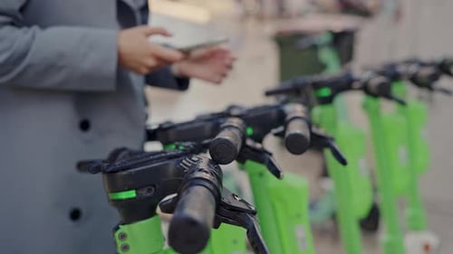 Woman Uses Phone Near Electric Shared Scooters