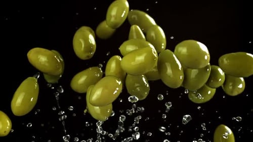Green Olives Suspended in the Air on Black Backdrop