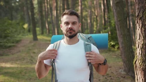 Porträt Hübscher junger Wanderer, der im Wald steht und den Kopf dreht und im Sonnenlicht lächelt