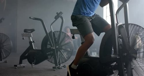 Determined biracial man training hard on elliptical bike at gym, slow motion