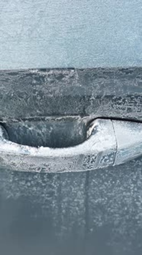 Close-up of a car door handle covered in frost and ice crystals on a cold winter morning, showing