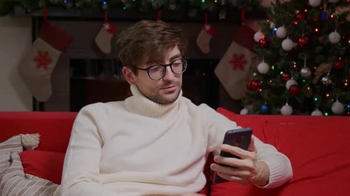 A man close up on a video call on the phone in a Chrismtas decorated scene.