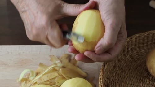 Adult Peels Potatoes at a Cutting Board