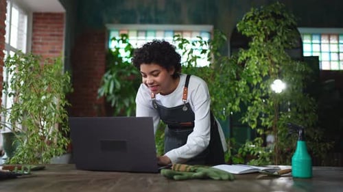 African Woman Florist Gardener Working in Botanical Store Using Laptop Order Plants Communicating on