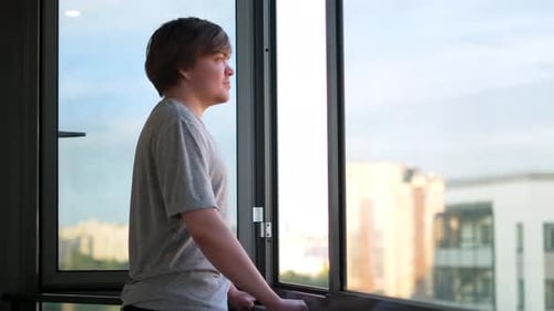 Young Man Looking Out Window at City View