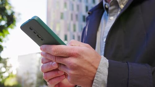 Man Typing on Mobile Phone in City Setting