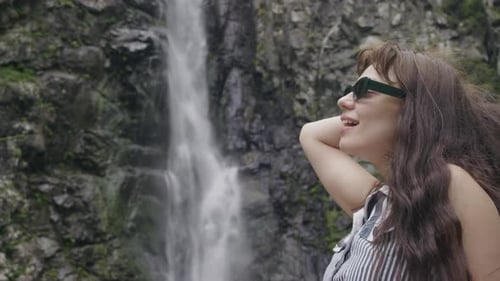 Closeup Shot of a Young Woman's Face Set Against the Backdrop of a Massive Waterfall Among Rocky