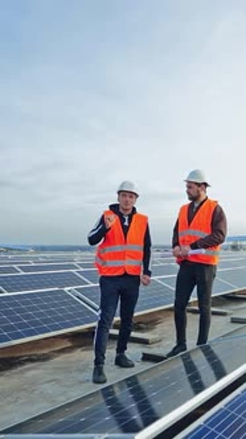 Blue solar panels on the field. Workers in the protective uniform on the modern photovoltaic farm.