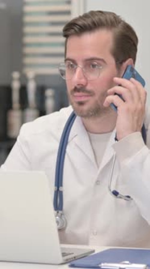 Male Doctor Using Phone and Laptop in Office