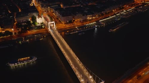 High Angle View of Vehicles Driving on Bridge Over River in City at Night Lighted Streets and