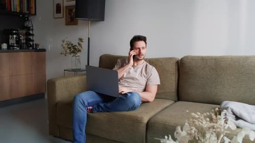 Young Man Talking on Phone with Laptop on Couch