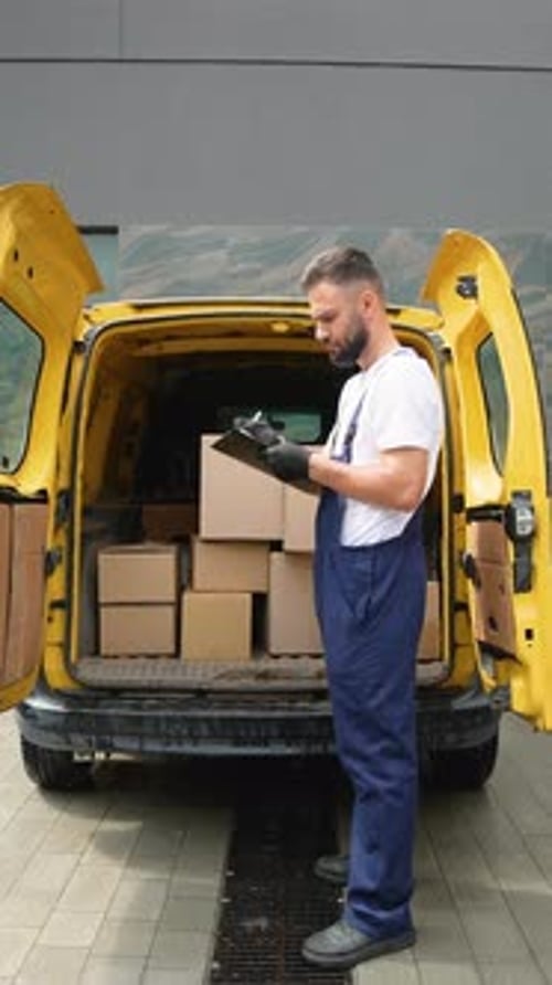 Delivery Man Reads Clipboard by Van with Boxes