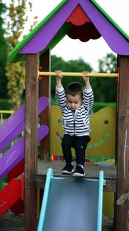 Caucasian kid waves on the horizontal bar and goes down by the slide.
