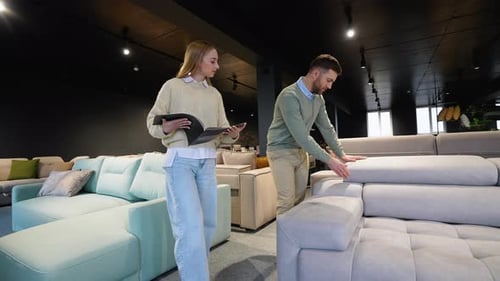 Young Couple Chooses Sofa with Catalog in Furniture Shop