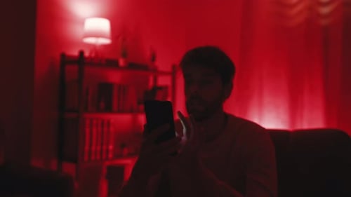 Young Adult Using Smartphone Under Colorful Lights At Home