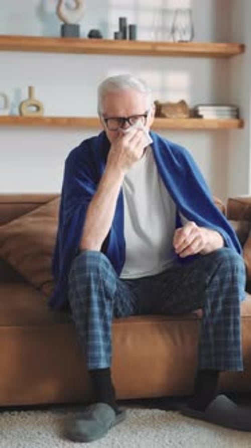 Vertical Portrait of Elderly Sick Man with Cough and Runny Nose Granddad Sitting on Couch in Cozy