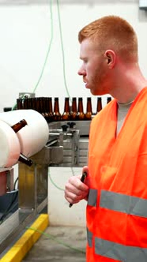 Brewery Worker Inspecting Beer Bottling Production Line