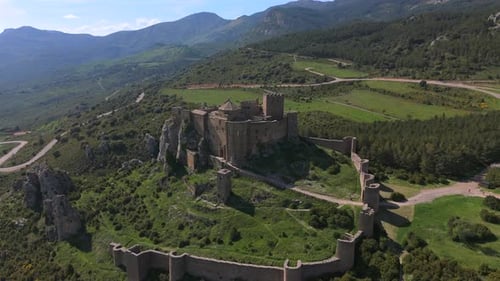 Drone orbit of medieval hilltop castle with defensive walls in mountainous rural landscape, clear da