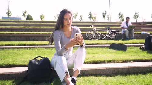 Female College Student Using Smart Phone in Sunny Campus Amphitheater Adult