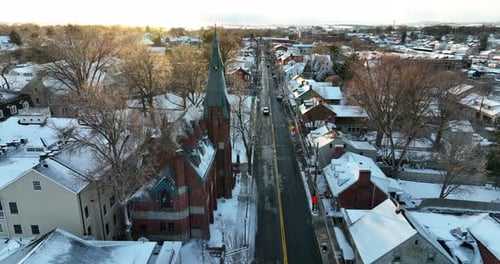 Lititz Pennsylvania USA church and neighborhood covered in winter snow at sunset. Aerial with golden