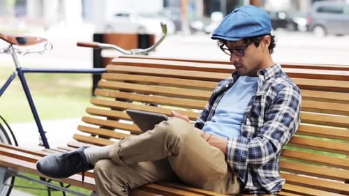 Creative hispanic man browsing on tablet with fixed gear bicycle in city street