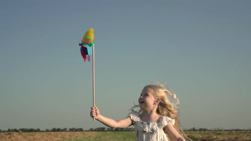 Happy Child Girl Runs Through a Rural Field with a Windmill