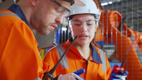 Young engineer man and woman talking and explaining about robot arms technology at factory.