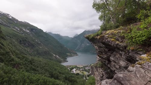 Timelapse of beautiful scenery on the cliff of a mountain, looking over mountains and a large lake.