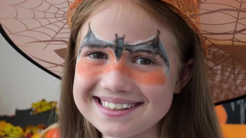 Girl Smiles Wearing Face Paint and Halloween Hat