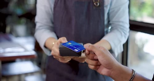 Close up credit card payment between customer and elderly cafe owner in apron holding card reader,