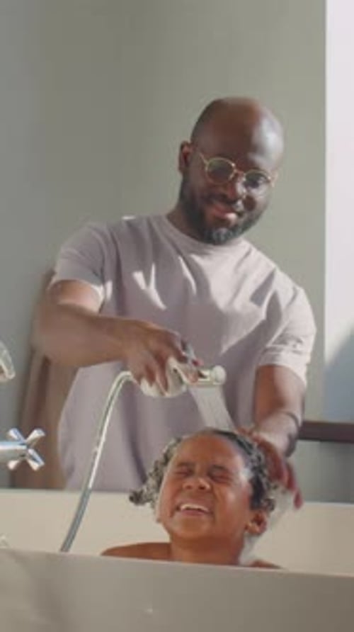 Father washing child's hair in bathtub at home
