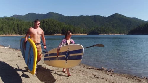 Couple Walking by Lake with Stand Up Paddle Boards Activity