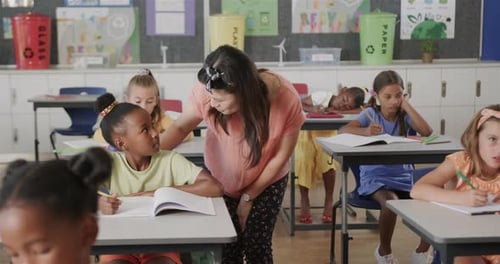 Glückliche, vielfältige Lehrerin hilft Schulmädchen am Schreibtisch in der Grundschulklasse, Zeitlupe
