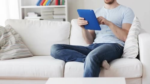Man Using Tablet Relaxing on White Sofa Indoors