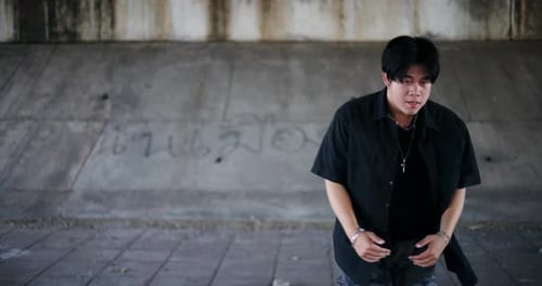 A stylish young man performs a freestyle dance under a footbridge in the city.