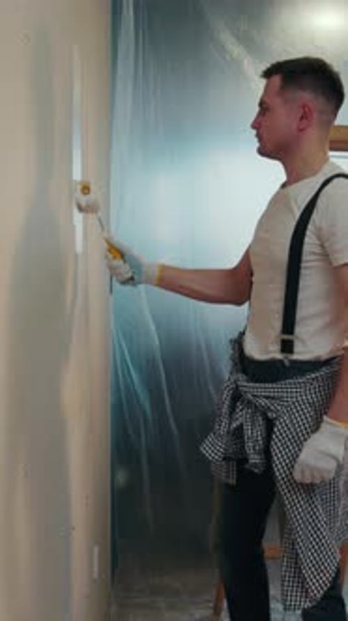 Attractive Young Man in a Casual Outfit in the Process of Wall Painting He Uses a Professional Tools