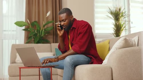 Serious African American Businessman Talking on Phone Use Laptop Working From Home Office Freelancer
