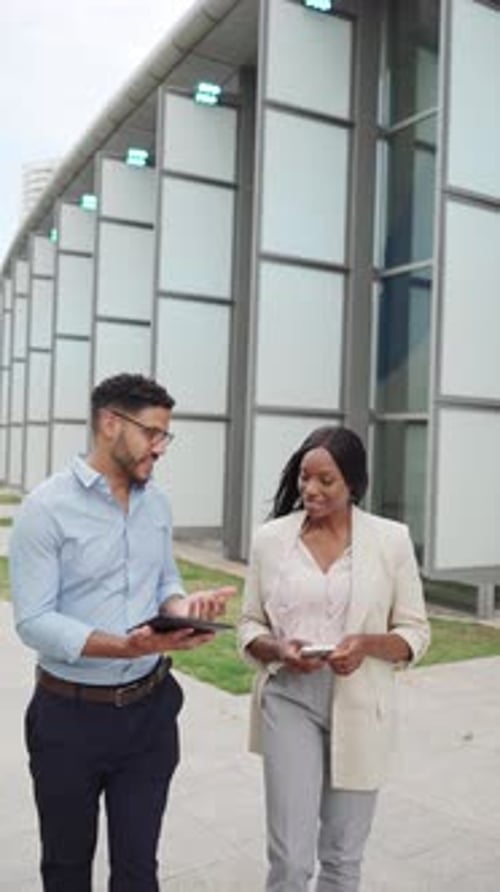 Vertical video of two multiethnic diverse business people walking outside office using digital table