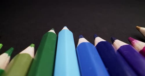 Macro probe low angle pov of colored pencils set on black background. Panning close up