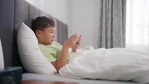 Boy Relaxing in Bed Using Smartphone