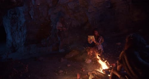 Tribe Cavemen Neanderthals Wearing Animal Skin Use Tablet Computer Sitting By the Fire in a Cave