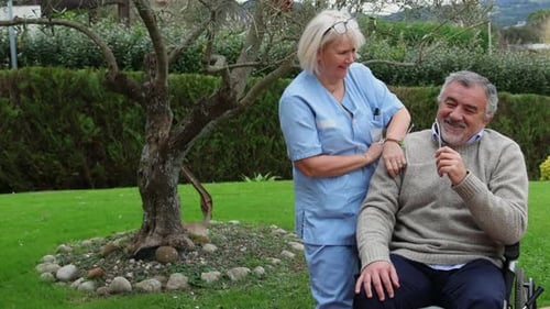 Nurse comforting elderly man in wheelchair in garden