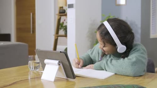 Female child in kitchen yawning taking notes, glancing at tablet, bobbing head to music, copy space