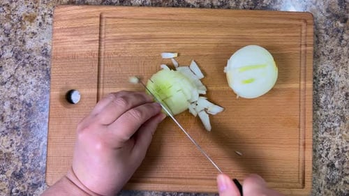 Cutting onions into small cubes with a knife on a wooden cutting board. Top view.