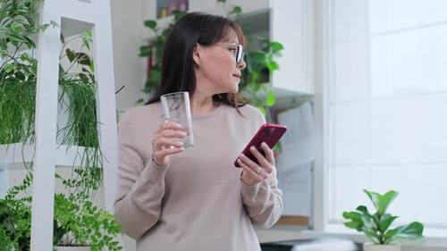 Woman Drinking Water While Using Smartphone Indoors