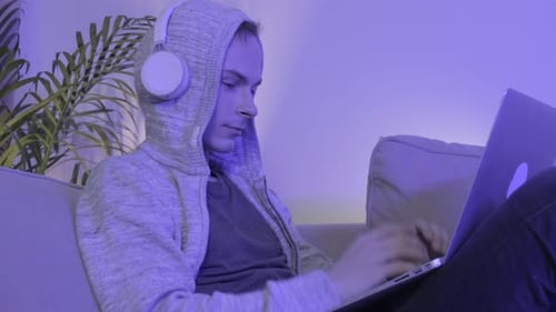 The Man Puts on Headphones and Lying on the Couch in the Evening Works