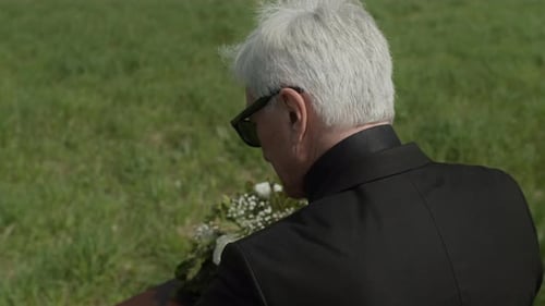 Senior with Hand on Coffin at Grave