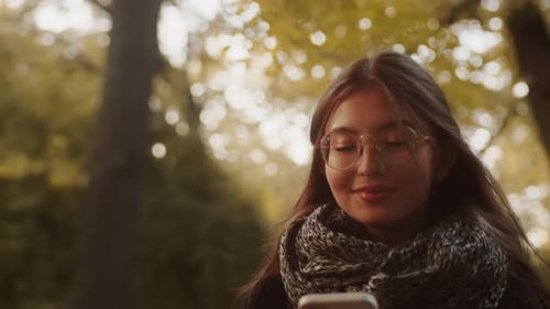 Portrait of a Happy Woman Smiling and Using Smartphone Walking in the Park in the Evening Caucasian
