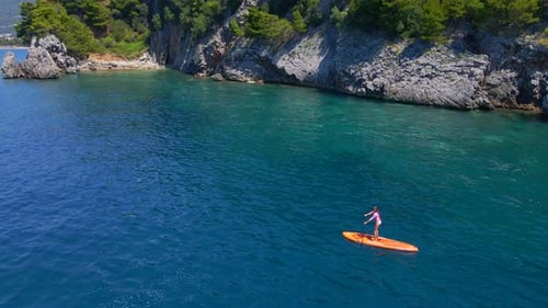 Young Woman on a Stand Up Paddle Board SUP Rawing Among Beatyful Rocks