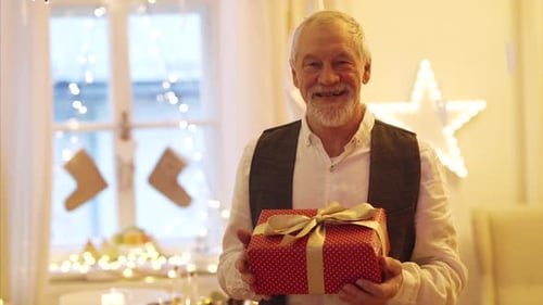Front View of Happy Senior Man Indoors Holding Present at Christmas